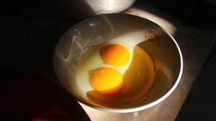 Close-up photo of 2 chicken egg yolks in a bowl in the morning sun.