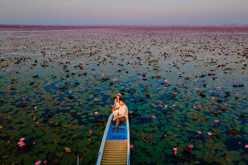 Drone aerial view at the sea of red lotus, Lake Nong Harn, Udon Thani, Thailand, a couple of men and woman in a boat at sunrise at the Red Lotus Lake in the Isaan