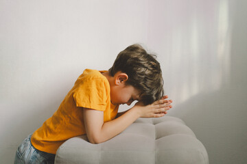 A boy in an orange T-shirt prays at home. Reading the Holy Bible. Concept for faith, spirituality...