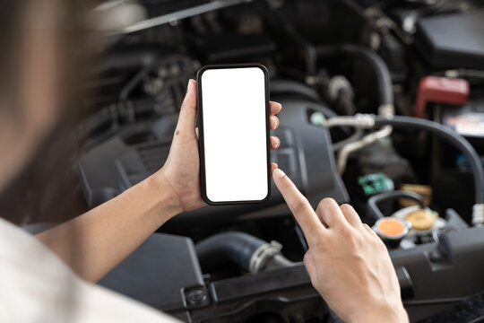 Close-up of woman's hands holding smartphone with empty space on screen for your text, background of car engine. - Powered by Adobe