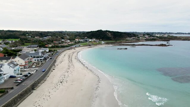 Cobo Bay Guernsey flight over golden beach crystal clear sea rocks and seafront including The Rockmount and Cobo Bay Hotel on calm sunny day