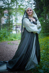 Adult mature woman 40-60 in a green long fairy dress in forest. Photo shoot in style of dryad and queen of nature. Fairy who loves nature in beautiful green summer forest. Concept of caring for nature