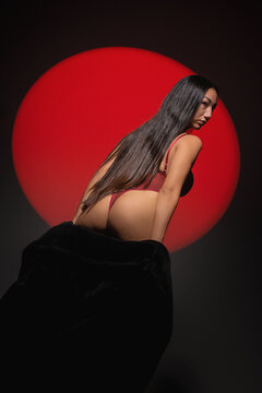 Beautiful asian girl in lingerie and fur coat posing on the gray background in the red lights. Beauty and fashion.