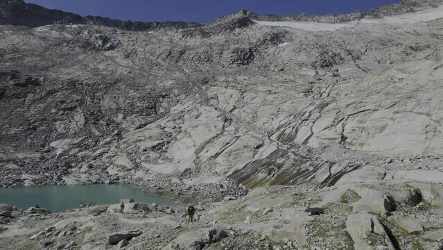 Hikers by a glacial lake with water flowing on uniquely shaped granite, Neves-Nofesferner glacier afar. South Tyrol's Alpine landscape.