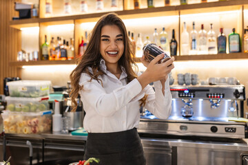 Young female worker at bartender desk in restaurant bar preparing cocktails with shaker. Beautiful...
