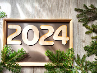 Wooden figures and numbers of the new year 2024 with frame and fir branches of Christmas tree....