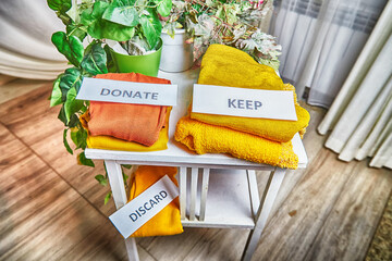 Signs with the words keep, donate, discard and fashion clothes folded in stacks in cozy room. The...