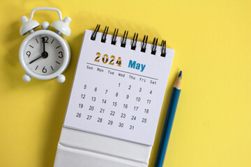Desk calendar for May 2024 and a small alarm clock on a yellow background.