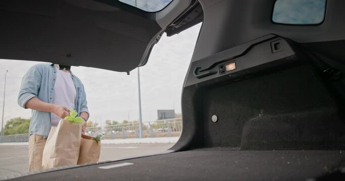 Young man opens Car Trunk and puts in bags with Groceries