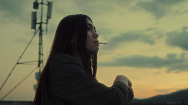 A profile portrait of a young brunette woman smoking cigarette at rooftop with a sky view