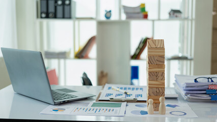 Laptop and financial graph documents on businessman's desk with wooden toys following steps of increasing graph. Ideas for the process of successful business growth.