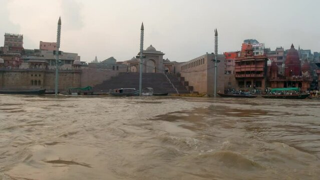 Cinematic Ganges still calm muddy brown River cruise chowk canal boat Varanasi Northern India State Ancient Holy city Khidkiya Ghat Pradesh Provinc landscape gray cloudy afternoon follow motion right