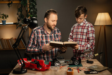 Father and son repairing a machine on the control panel, working at home, reading a book on...