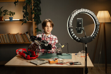 Teen boy soldering sits in his room. Blogger makes online streaming using smartphone and talking why soldering and tools.