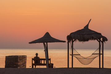 woman sitting on a bench near a hammock waiting for the sunrise at the red sea