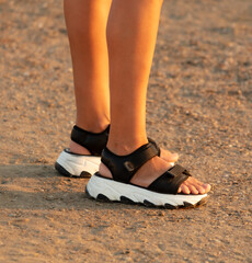 Legs of a girl in sandals on the ground. Sunset