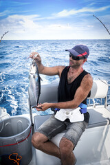 Tough man wearing baseball cap on board ship while fishing against blue sea background.