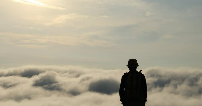 The silhouette of backpackers taking pictures on mountain peak above clouds, tourists with beautiful moving clouds.
