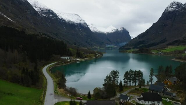 aerial view of a car moving on an asphalt road highway on the shore of Oldevatnet blue mountain lake with mountains covered with snow on background in norway
