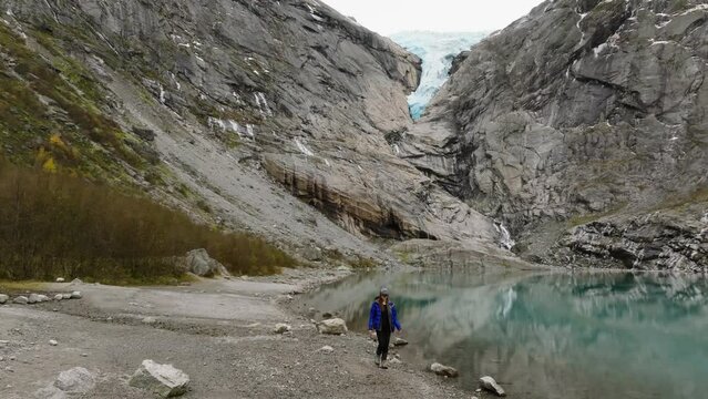 aerial view of a walking woman tourist hiker on rocky shore of briksdalsbreen glacier blue lake in norway