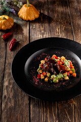 Braised beef cheeks with a vibrant vegetable ratatouille, served on a rustic black plate, autumn harvest-inspired