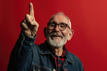 Obraz premium Ecstatic Senior Man Expresses Joy With Raised Finger Against Vibrant Red Background ()
