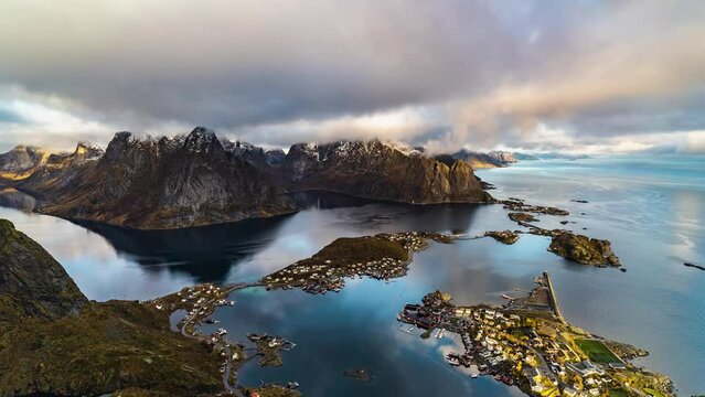time lapse of fast moving clouds over olstinden mountain and reine village with reflections in water of Kjerkefjorden fjord on lofoten islands in norway, view from Reinebringen mountain