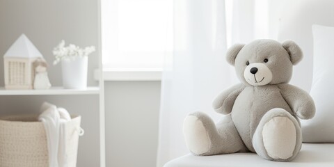 A gray teddy bear sits on a white sofa, with blurred white home decor in the calm and bright background.