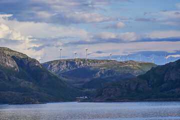 Modern windmills for production of electric energy from wind on the top of mountain ridge in norwegian fjord. Example of green, sustainable and carbon neutral electric energy from renewable resources.