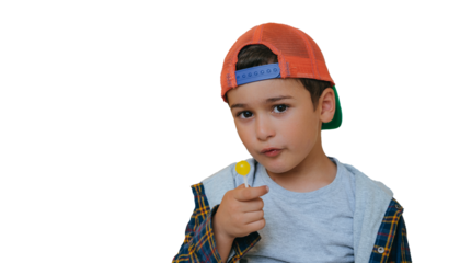 Little caucasian boy in baseball cap and plaid shirt holds lollipop looks at camera with confident face expression with copy space on background. Cute male kid loves candy and sweets. Mockup.