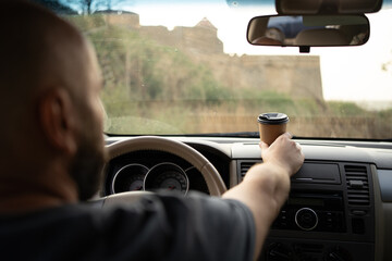 Coffee in the car. Bearded man driving a car and drinking coffee while driving, placing a paper...