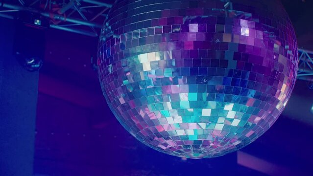 A large disco ball is spinning against the background of the stage with lighting devices illuminating it with colored rays of light. A beautiful glass ball at a renault dance party at the club