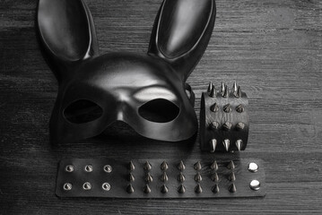 Black rabbit mask and studded leather bracelets on the black wooden table close up background.