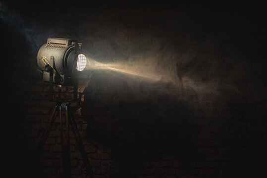 Old retro style theater spotlight in the smoke on the brick wall background with copy space. Cinema.