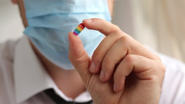 Man in medical mask and suit holding a pill in the colors of the rainbow LGBT