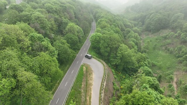 Ascending drone footage of a car driving on the Castle Road on a foggy day in Bourscheid, Luxembourg