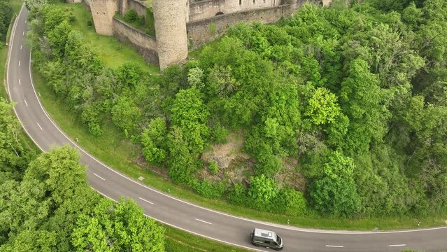 Ascending drone shot of a van car driving on the castle road near to Bourscheid Castle, Luxembourg