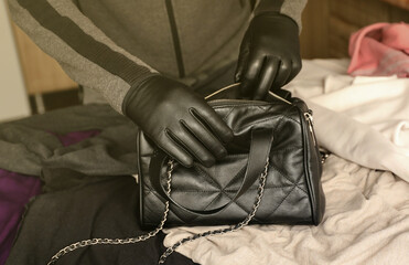 Robber in black outfit and gloves see on opened stolen women bag. A thief evaluates the value of...
