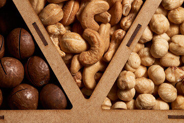 Close-up of unshelled macadamia nuts and shelled cashews and hazelnuts in a box. Top view.