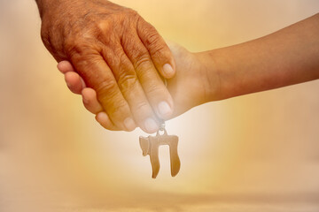 Am Israel Chai. Hands of an elderly man holding the hand of a child close up. they holding a silver Chai key chain, which spell "life" in Hebrew.