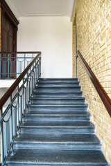 An old antique staircase in a historic building. An empty staircase and brick walls. Cast iron railings framed by wood.