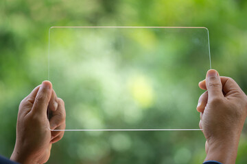 Hand holding and showing transparent tablet device. Business, natural green bokeh...