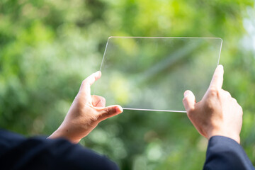 Hand holding and showing transparent tablet device. Business, natural green bokeh...