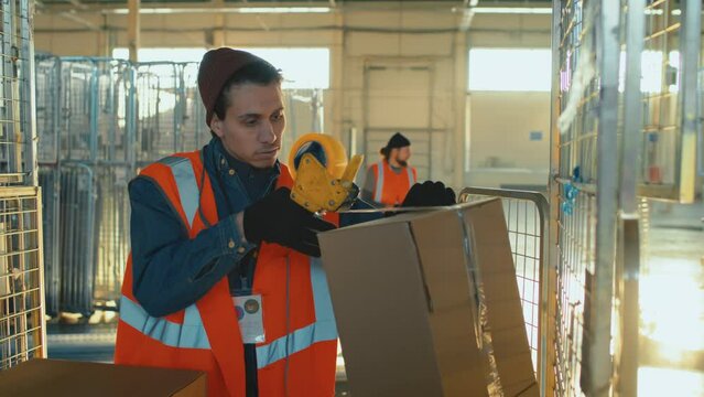 Medium shot of Biracial warehouse male worker closing box with duct tape during workday in spacious storage room