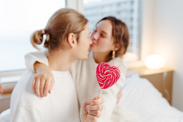 Young man and woman , happy couple kissing, hugging,  holding lollipop sitting at home, selective focus. Love concept  