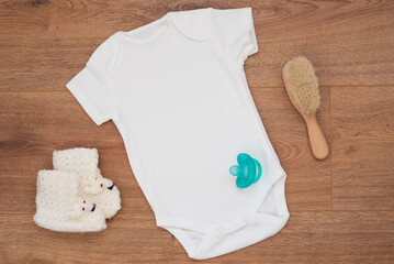 Mockup of white baby bodysuit on wood background with knitted booties. Blank baby clothes template mock up.