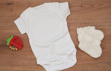 Mockup of white baby bodysuit on wood background with knitted booties. Blank baby clothes template mock up. Flat lay styled stock photo.
