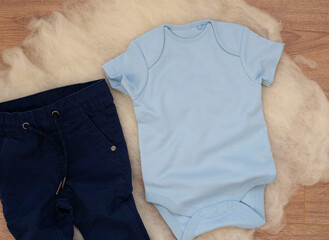 Mockup of blue baby bodysuit on wood background with jeans. Blank baby clothes template mock up. Flat lay styled stock photo.