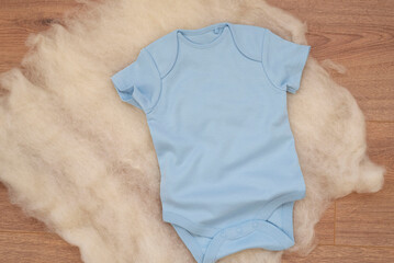 Mockup of blue baby bodysuit on wood background. Blank baby clothes template mock up. Flat lay styled stock photo.