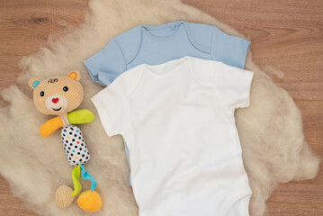 Mockup of white and blue baby bodysuit on wood background and colorful bear toy. Blank baby clothes template mock up. Flat lay styled stock photo.